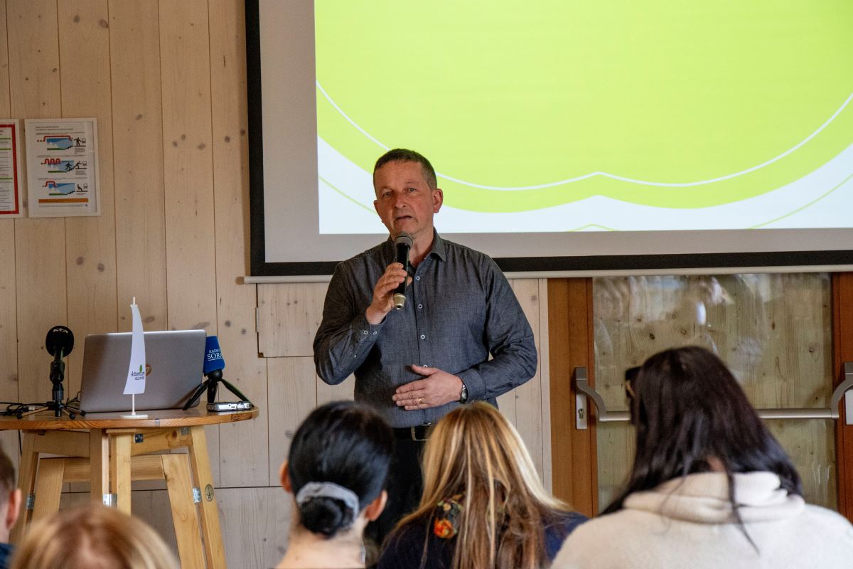 Matjaž Mastnak na novinarski konferenci v Arboretumu Direktor Arboretuma Volčji Potok Matjaž Mastnak nagovarja zbrane na novinarski konferenci v notranjem prostoru Arboretuma. Ob njem sta mikrofon in prenosni računalnik, v ozadju pa je projekcijsko platno, medtem ko občinstvo spremlja predstavitev.