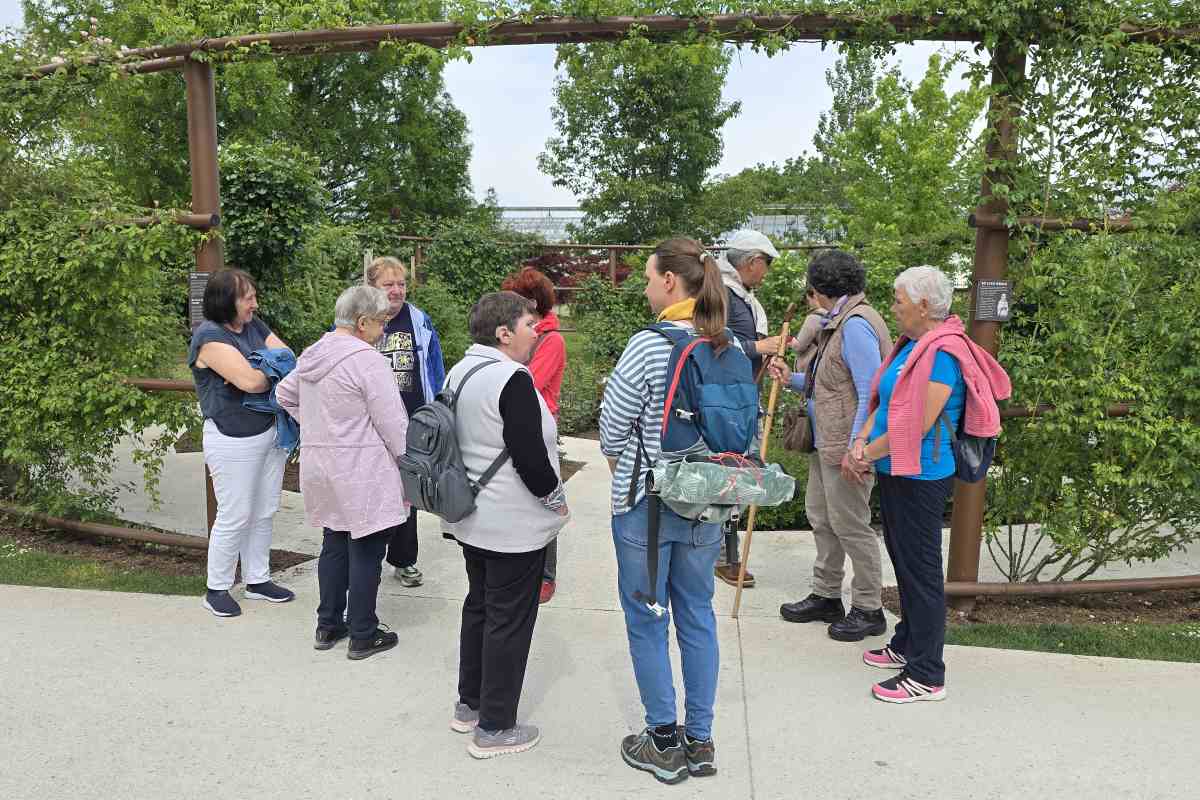 V Rožnem vrtu papeških vrtnic Skupina udeležencev stoji v rožnem vrtu ob oporah za vrtnice in posluša razlago.
