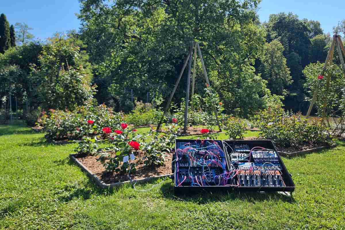 Cvetlični orkester Modularni sintetizator v odprtem kovčku stoji na travi med rožnimi gredami v Arboretumu Volčji Potok.