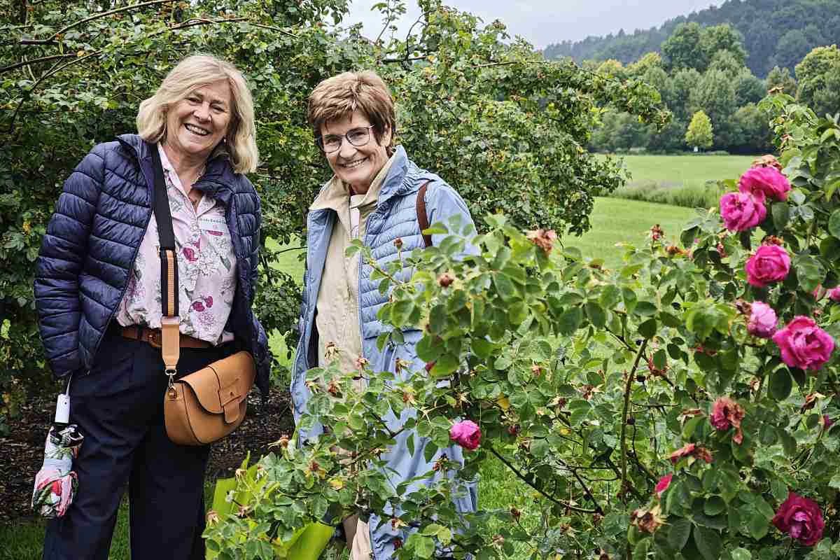 Srečanje ljubiteljev vrtnic Dve udeleženki Mednarodnega foruma o vrtnicah stojita ob cvetočem grmu rožnatih vrtnic v Arboretumu Volčji Potok.
