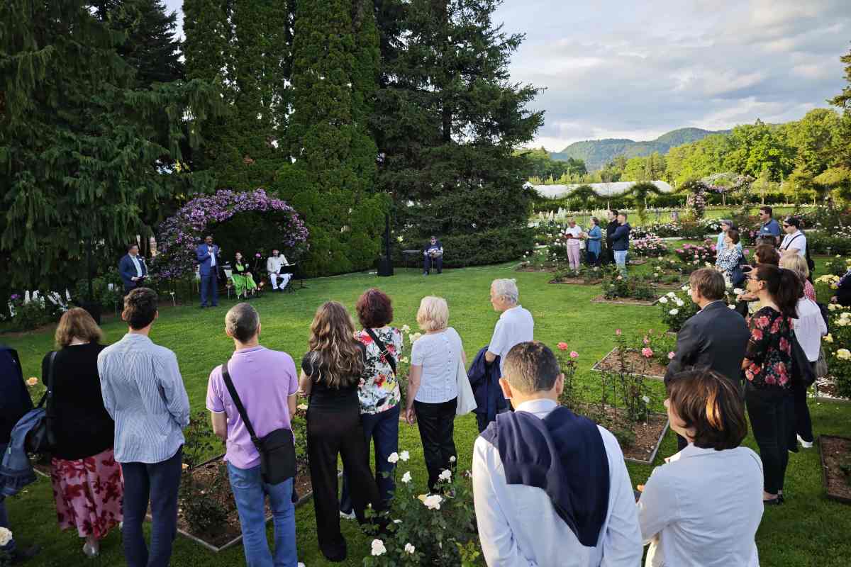 Udeleženci Mednarodnega foruma o vrtnicah stojijo v Zgornjem rozariju Arboretuma Volčji Potok in poslušajo nagovor med cvetočimi vrtnicami.