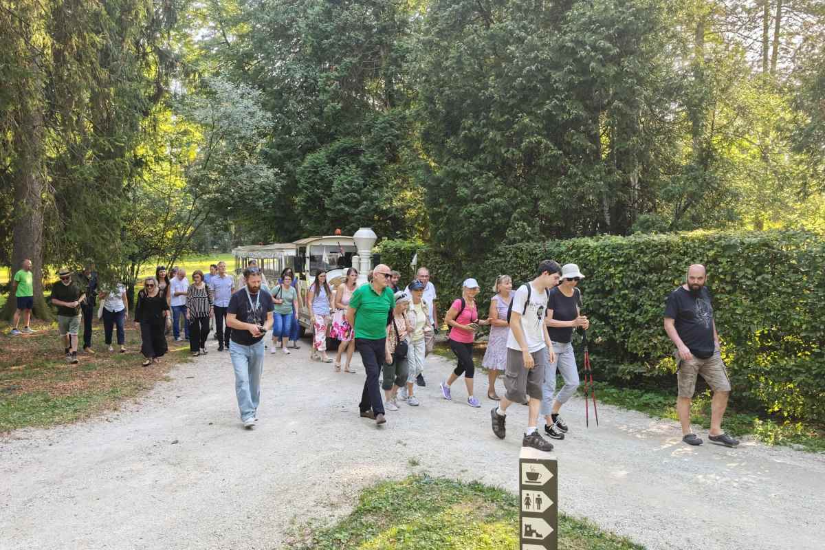 Obiskovalci na vodenem ogledu razstave Skupina obiskovalcev se sprehaja po Arboretumu Volčji Potok med vodenim ogledom taktilne razstave.