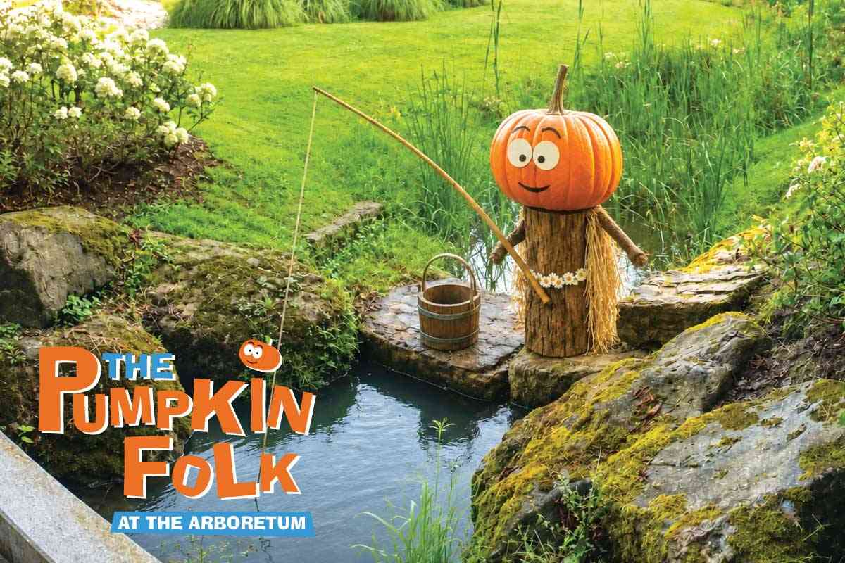 One of the Pumpkin Folk on a Mysterious Fishing Trip A Pumpkin Folk character with an orange pumpkin for a head stands beside a stream with a fishing rod and a wooden bucket. Below is the text “The Pumpkin Folk at the Arboretum.”