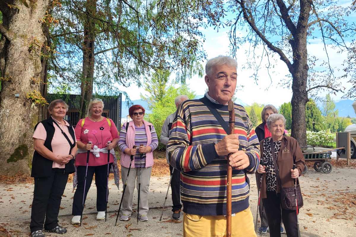 Ludvik Travnik z leseno palico v rokah govori skupini udeležencev v parku.