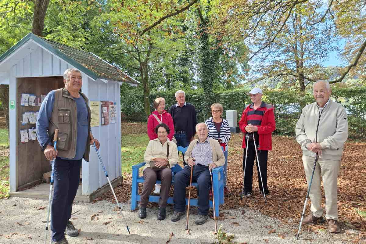 Udeleženci septembrskega Sprehoda z Modro palico Skupina udeležencev s pohodnimi palicami ob modri klopci v Arboretumu Volčji Potok.