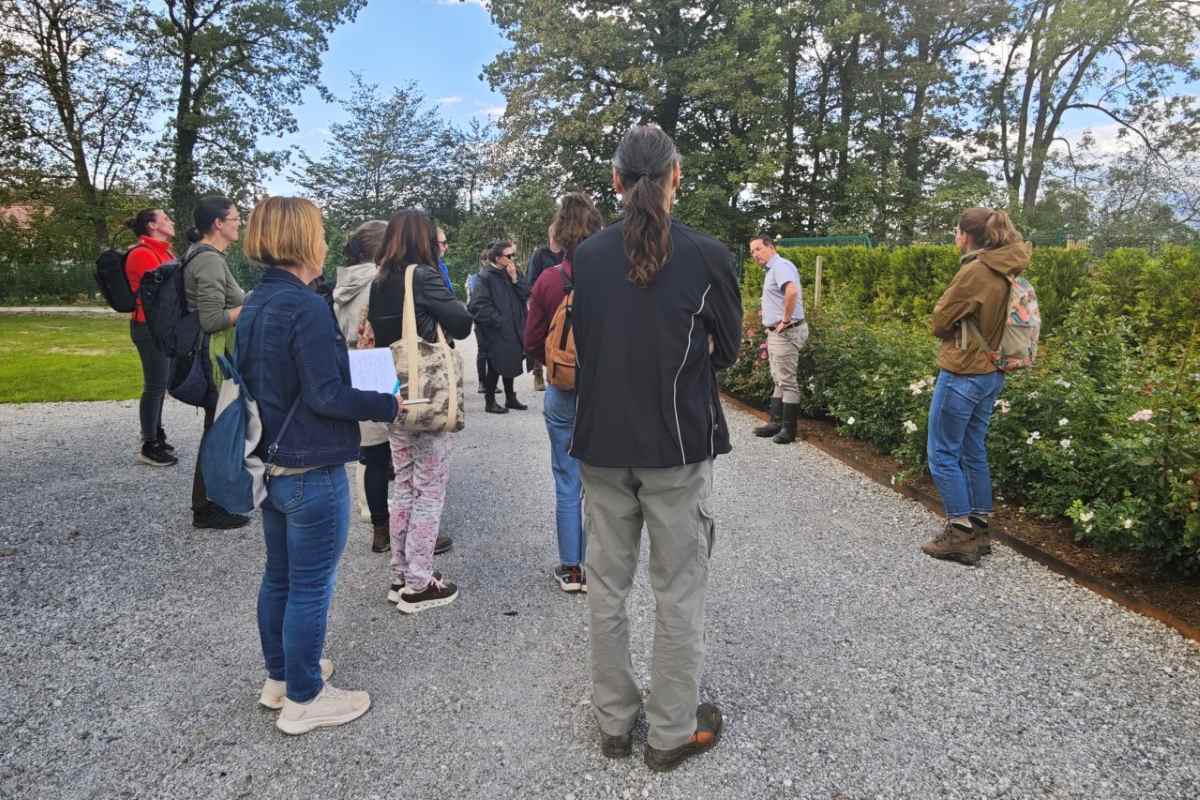 Strokovna izobraževanja: direktor Matjaž Mastnak deli znanje Direktor Arboretuma Matjaž Mastnak ob parkovni zasaditvi predava skupini udeležencev, ki stojijo na peščeni poti.