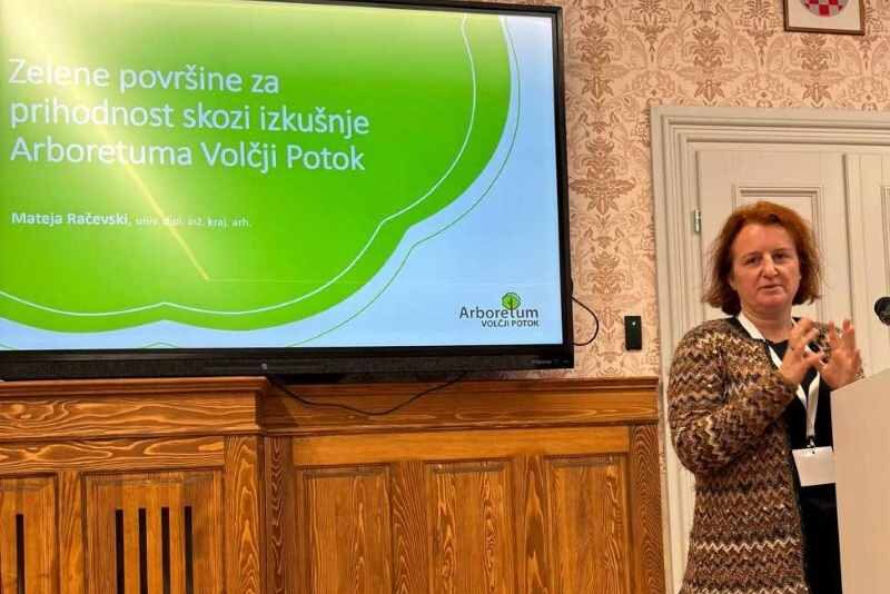 Mateja Račevski na konferenci GREEN DAYS Mateja Račevski ob govorniškem pultu in zaslonu z naslovom predavanja Zelene površine za prihodnost skozi izkušnje Arboretuma Volčji Potok.
