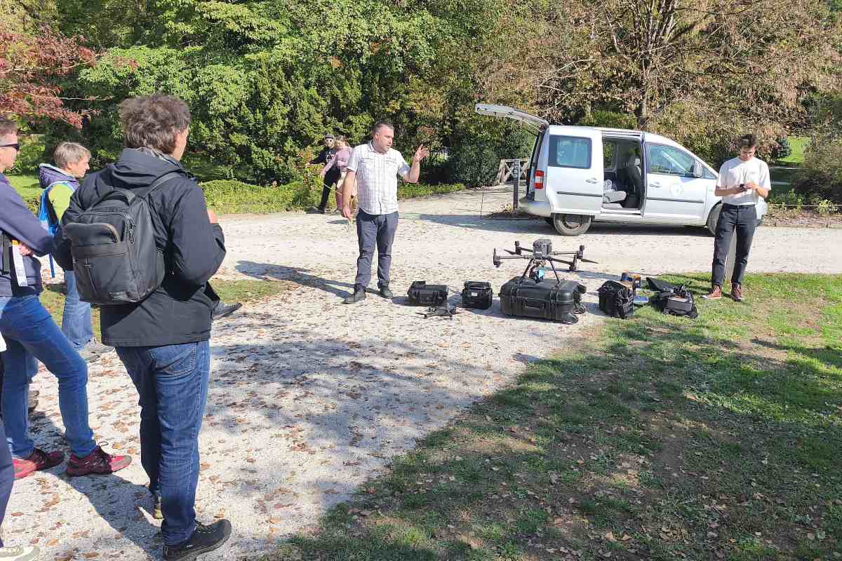 Predstavitev drona in opreme za spremljanje dreves. Foto: Nika Halaš Predavatelj na parkovni poti predstavlja opremo. Pred njim je na kovčku velik dron, ob njem pa drugi pripomočki.