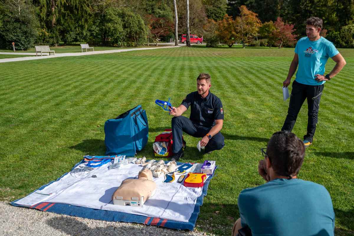 Predstavitev pripomočkov za prvo pomoč. Foto: Nika Halaš Izvajalec kleči ob podlogi z lutko za oživljanje, učnim defibrilatorjem in drugo opremo ter kaže pripomoček za prvo pomoč.