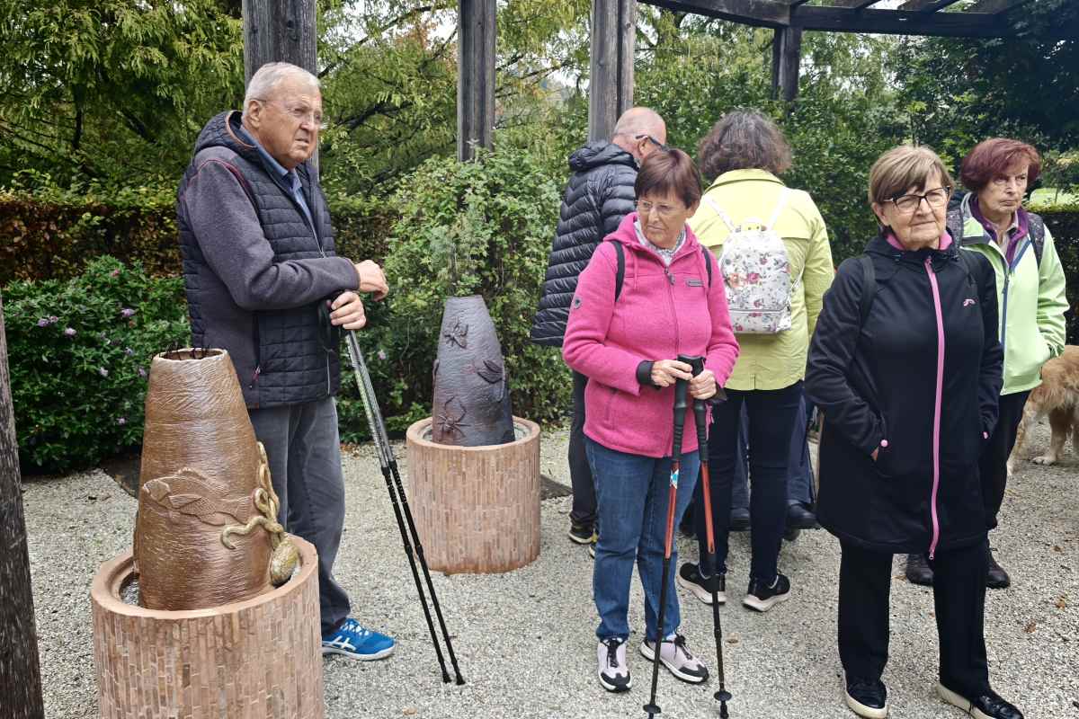 Keramične skulpture Varuhi narave v Dišečem vrtu Arboretuma Volčji Potok Udeleženci sprehoda z Modro palico si v Dišečem vrtu Arboretuma Volčji Potok ogledujejo keramični skulpturi iz cikla Varuhi narave. Skupina stoji ob umetniških delih, postavljenih med zelenje pod leseno pergolo.